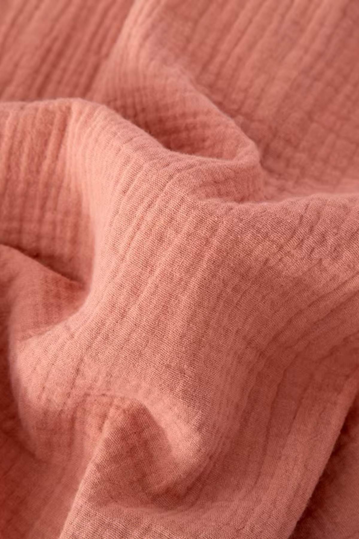 Tissu en coton rose doux, légèrement froissé avec des motifs en relief, évoquant une ambiance apaisante et chaleureuse