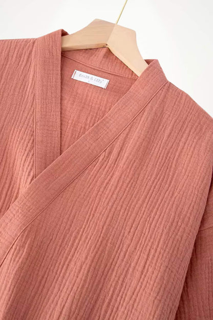 Peignoir kimono en tissu texturé rose, avec un col en V et des manches larges, suspendu sur un cintre en