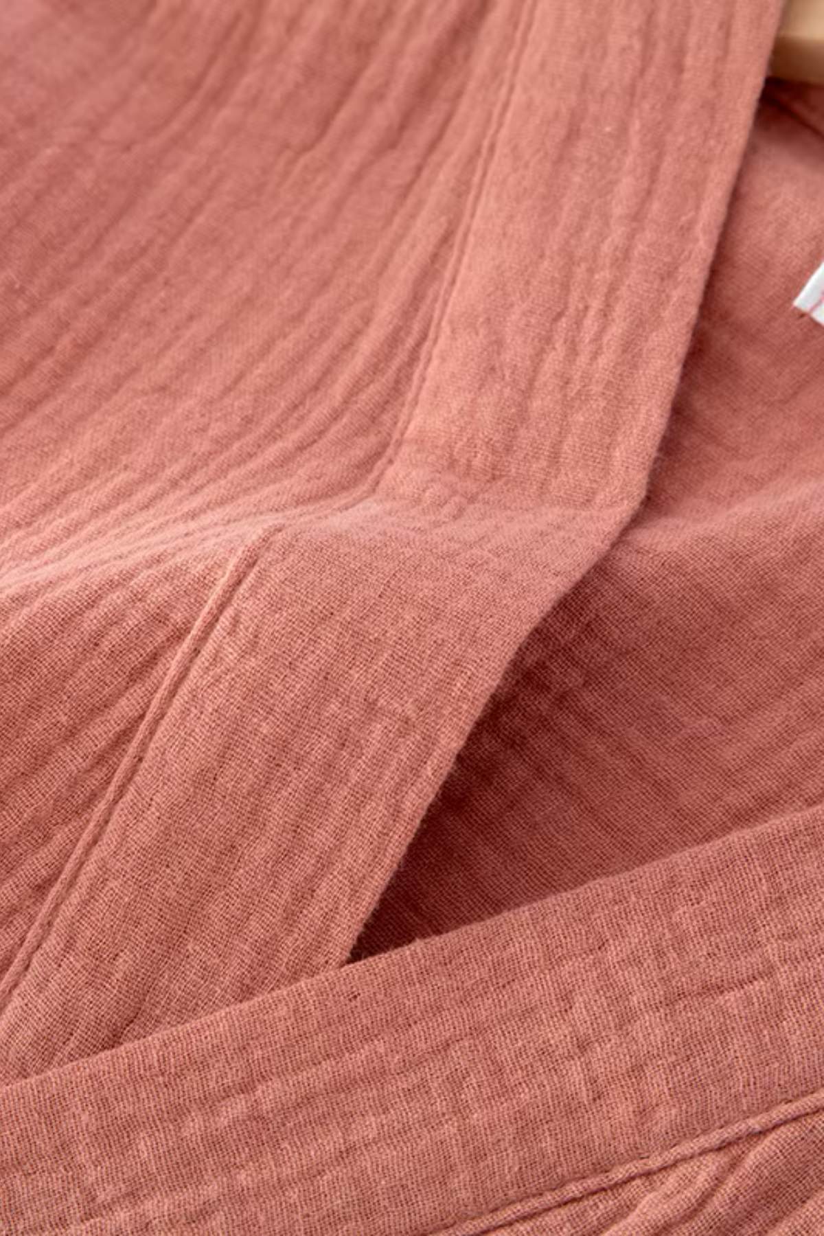 Peignoir kimono en tissu rose doux avec des motifs texturés, drapé élégamment sur une surface neutre