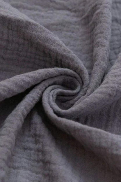 Tissu doux en coton gris, légèrement froissé, enroulé en spirale, évoquant un style japonais apaisant
