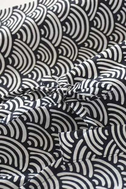 Tissu en coton noir avec motifs ondulés blancs, plié avec un nœud décoratif au centre