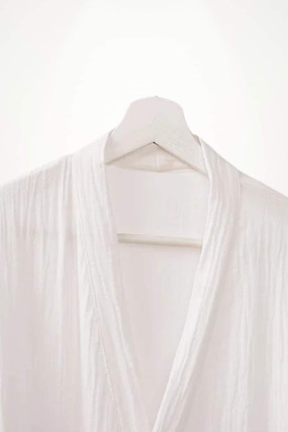 Peignoir kimono blanc suspendu sur un cintre en bois, avec un tissu léger et des plis délicats