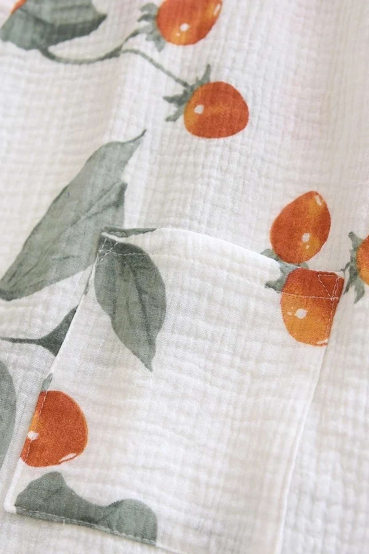 Tissu en coton blanc avec des motifs de cerises orange et des feuilles vertes, texture légère et douce