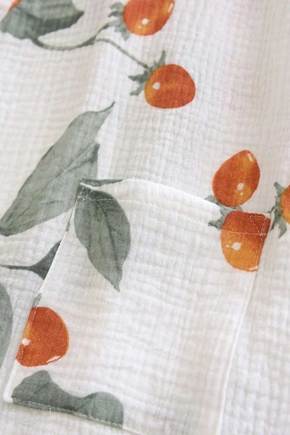 Tissu en coton blanc avec des motifs de cerises orange et des feuilles vertes, texture légère et douce