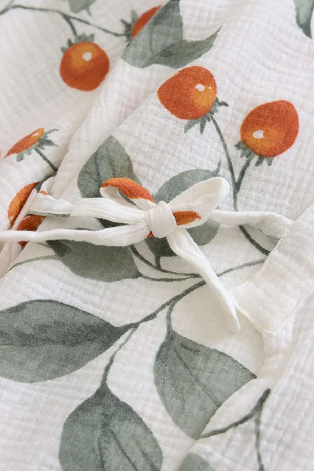 Tissu en coton blanc avec motifs de cerises orange et feuilles vertes, noué avec un cordon blanc