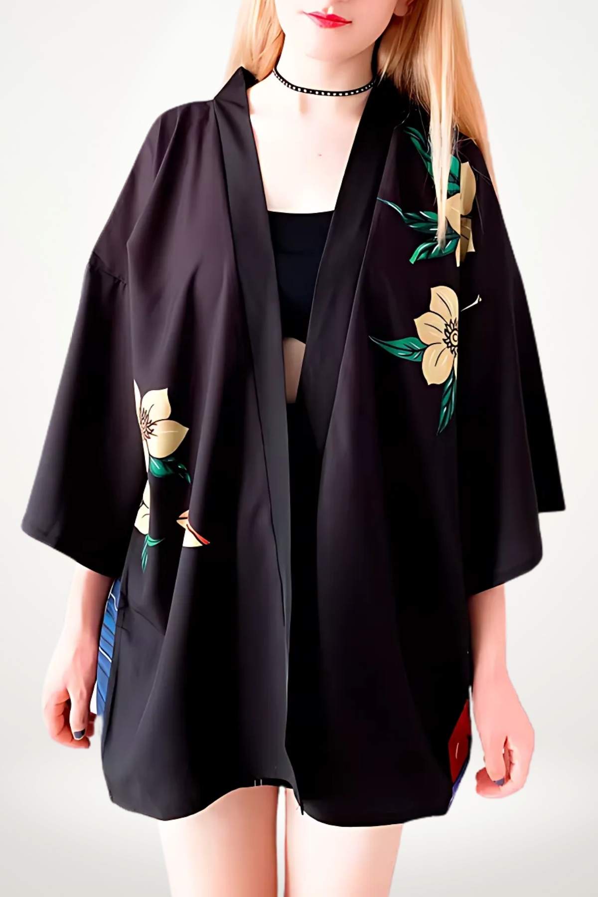 Veste kimono noire avec motifs floraux jaunes, portée par une femme, fond neutre et posture décontractée