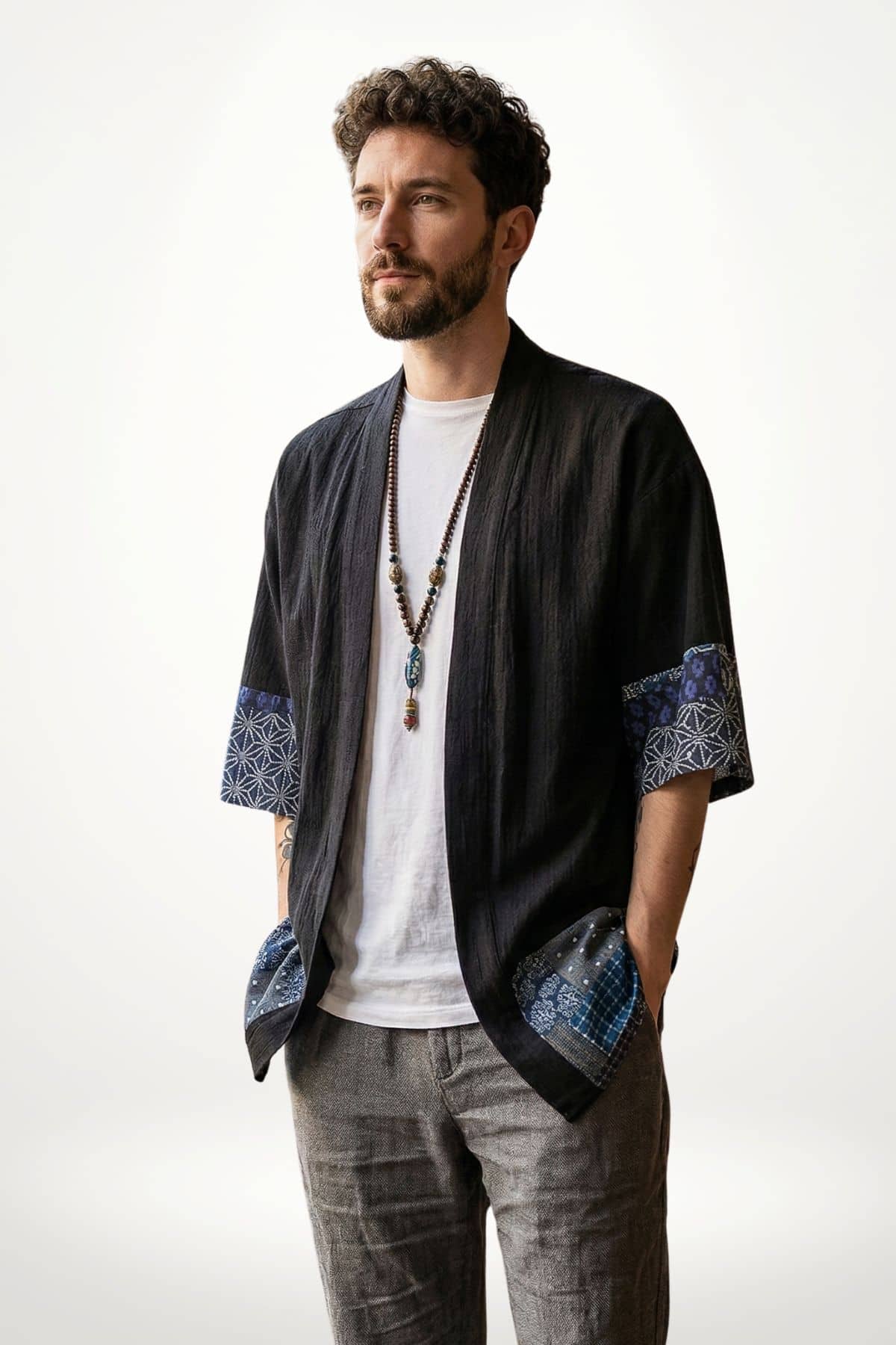 Homme portant une veste style kimono noire avec des motifs bleus, devant un fond clair, affichant une posture décontractée